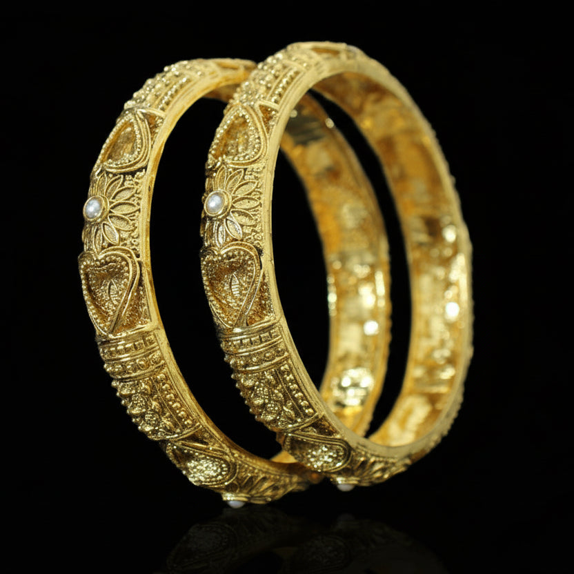 Two gold bangles with intricate designs on a gray background, featuring the brand 'SAHELI'.