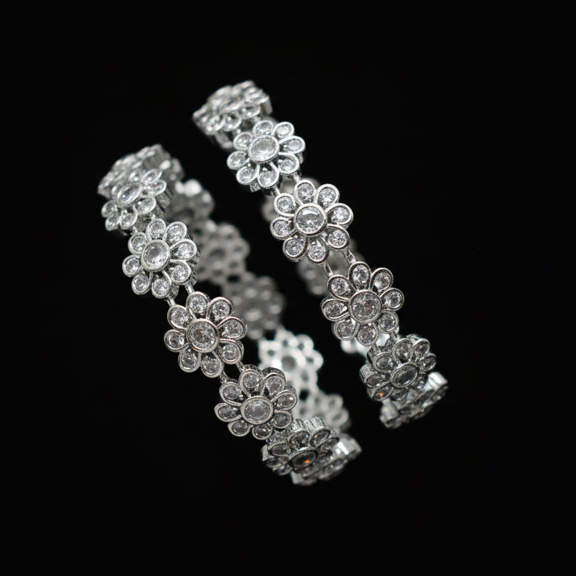 Silver floral bracelet on a gray cushion against a dark background