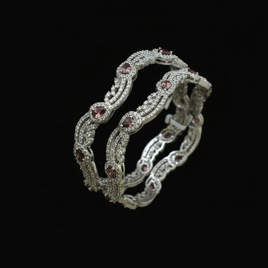 Pair of silver bangles with gemstones on a dark background, branded 'Saheli'.