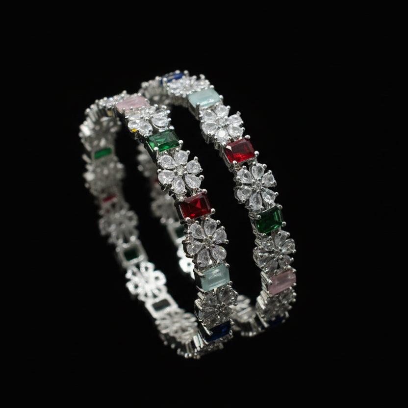 Two diamond bracelets with colored gemstones on a gray cushion against a dark background