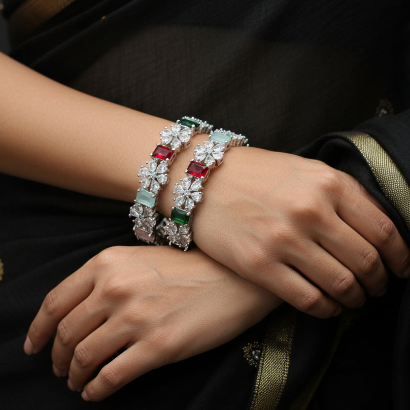 Two diamond bracelets with colored gemstones on a gray cushion against a dark background