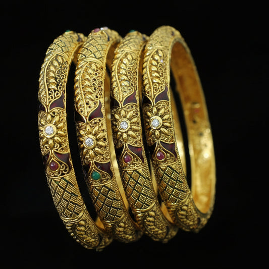 Set of gold bangles with intricate designs and gemstones on a black stand, branded 'Saheli'.