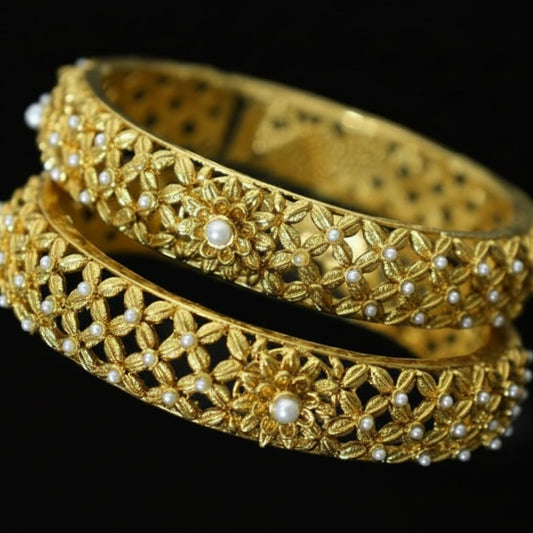 Gold bangles with intricate designs on a gray background, featuring the brand 'SAHELI'.