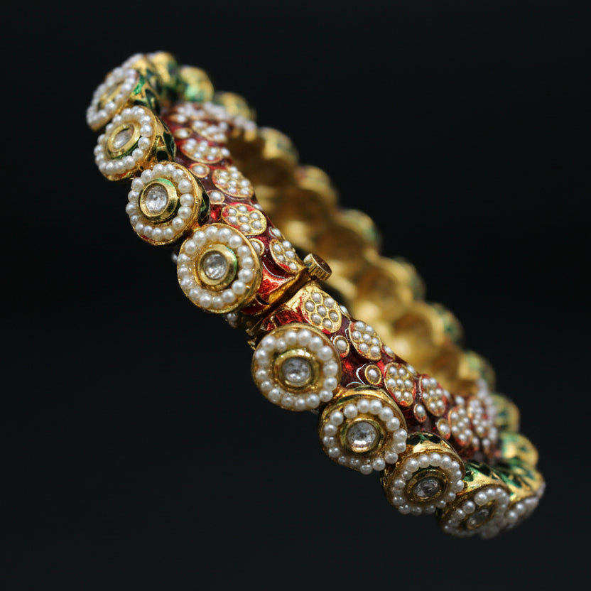 Decorative bracelet with pearls and gold accents on a gray stand