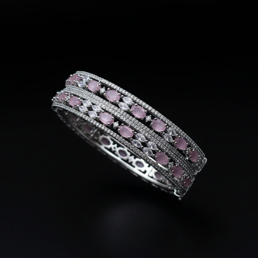 Two silver bangles with pink stones on a dark background, featuring the brand 'Saheli'.