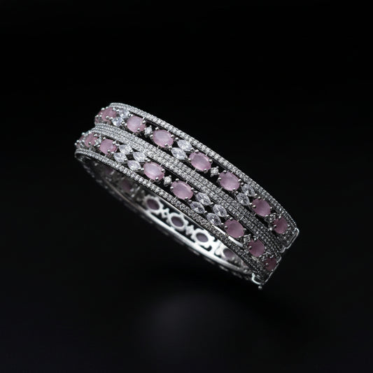 Two silver bangles with pink stones on a dark background, featuring the brand 'Saheli'.