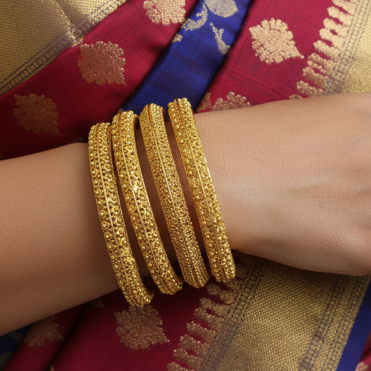 Set of gold bangles on a black stand against a gray background