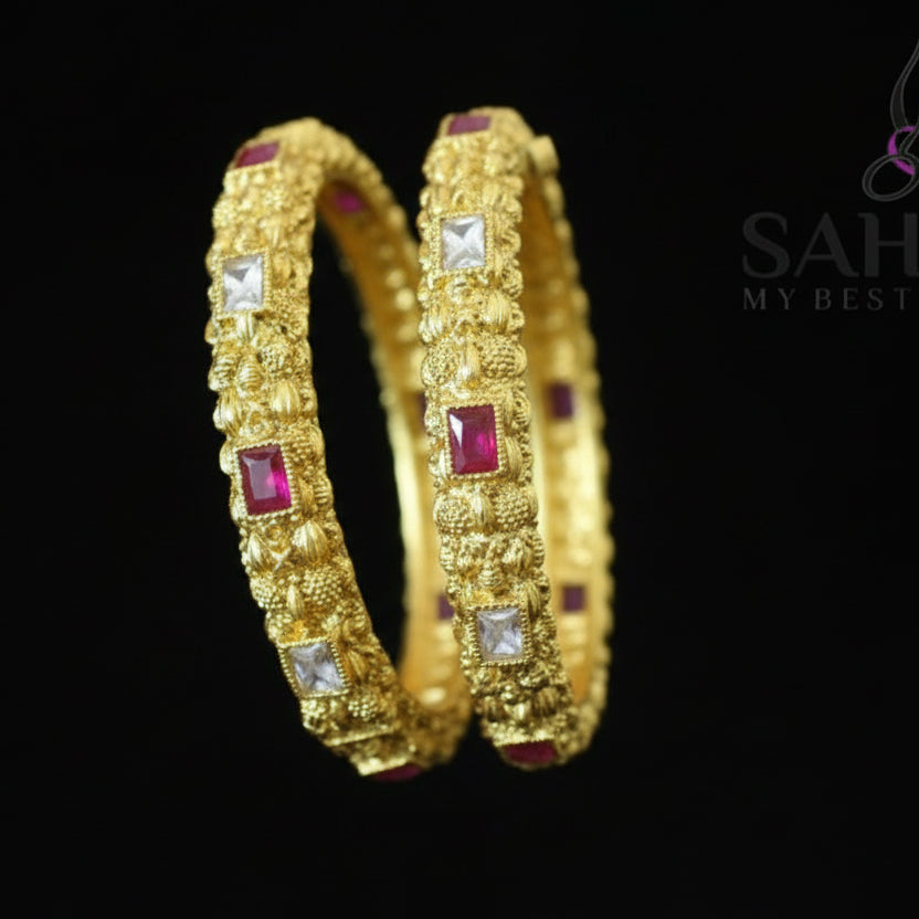 Gold hoop earrings with red stones on a black stand, branded 'Saheili'.