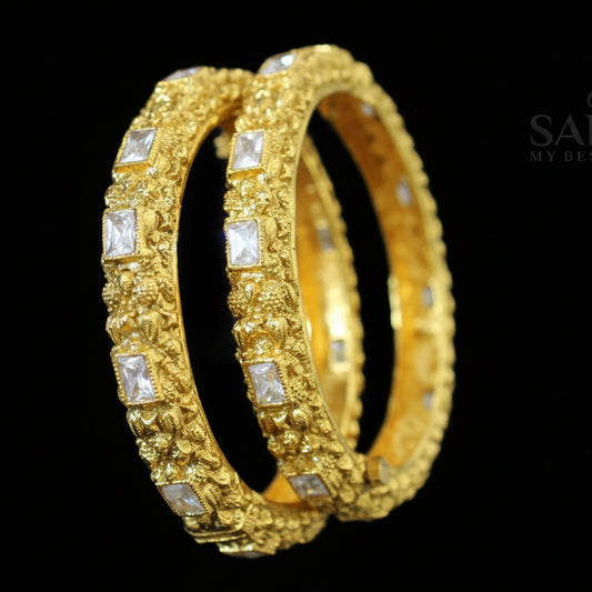Gold bangles with embedded stones on a dark background, featuring the brand 'Saheli'.