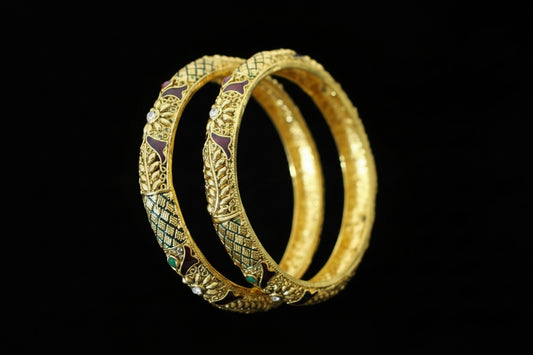 Gold bangles with intricate designs on a gray background, featuring the brand 'SAHELLI'.