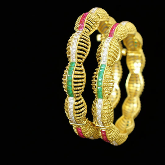 Gold bangles with green and red stones on a gray background, featuring the brand 'Saheli'.