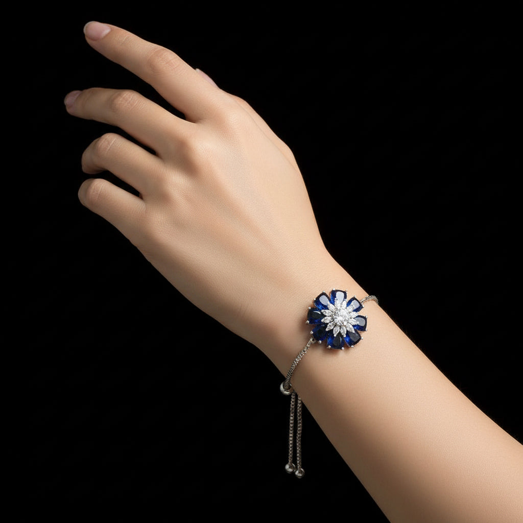 Silver bracelet with a blue and white floral clasp on a dark background, featuring the brand 'SAHELI'.