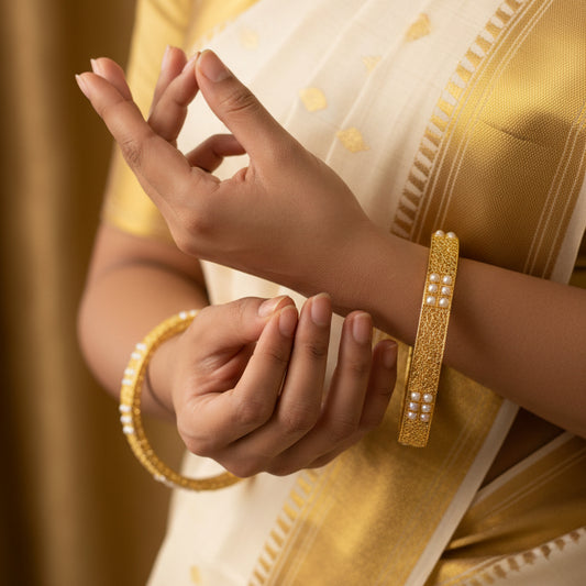Gold bangles with pearl embellishments on a dark background, featuring the brand 'Saheli by Heera Chand'.