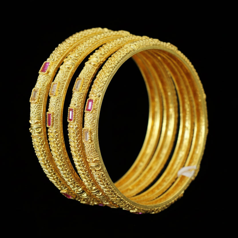 Set of gold bangles with red stones on a black stand, branded 'Saheli'.