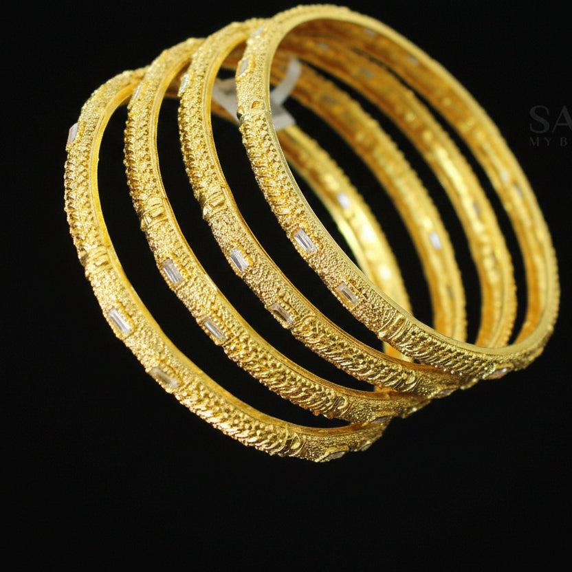 Gold bangles on a dark surface with 'SAHELLI' branding.