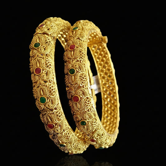 Gold bangles with intricate designs on a gray background, featuring the brand 'Saheli'.