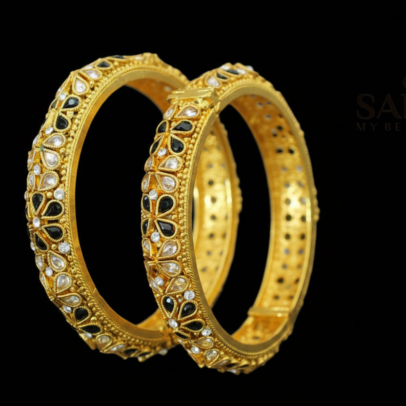 Gold bangles with intricate designs on a dark background, featuring the brand 'Saheli'.