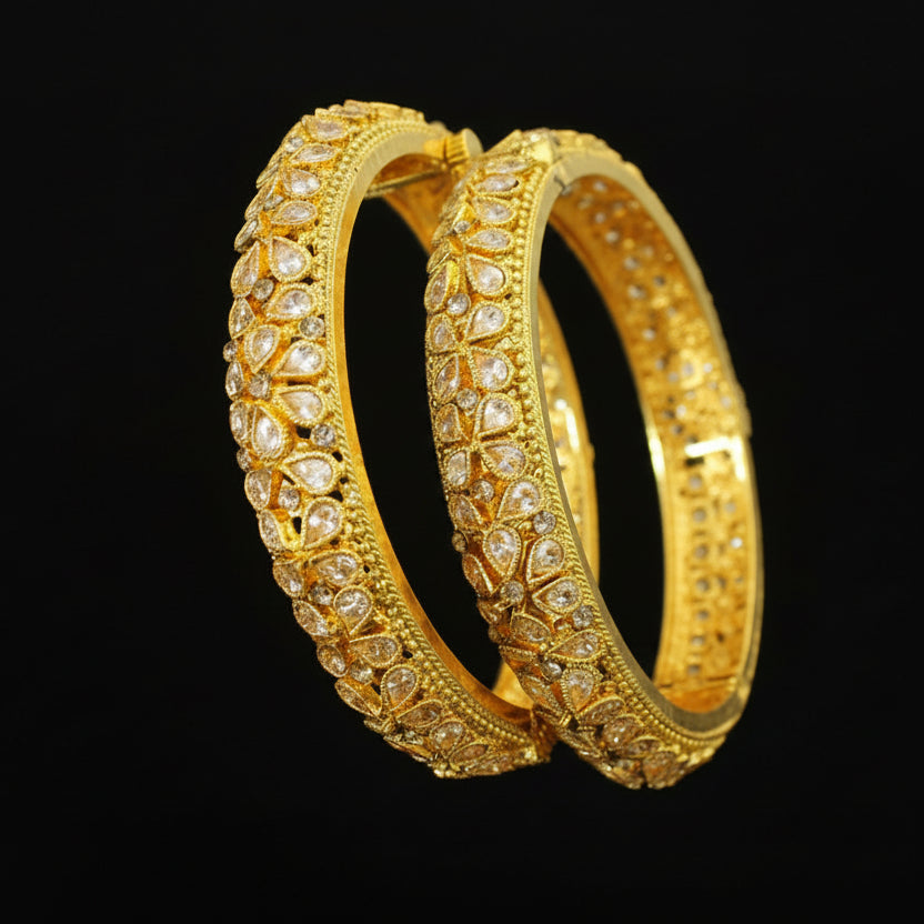 Gold bangles with diamond-like stones on a gray background, featuring the brand 'SAHELI'.