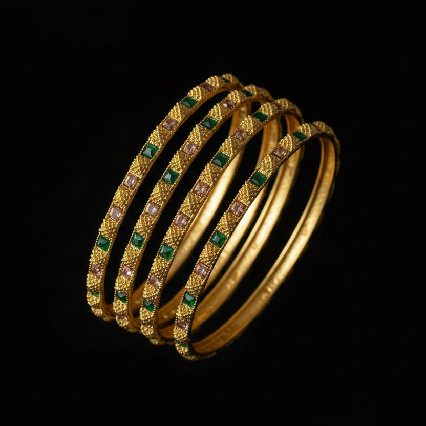 Set of gold bangles with green stones on a gray stand, branded 'Saheli'.
