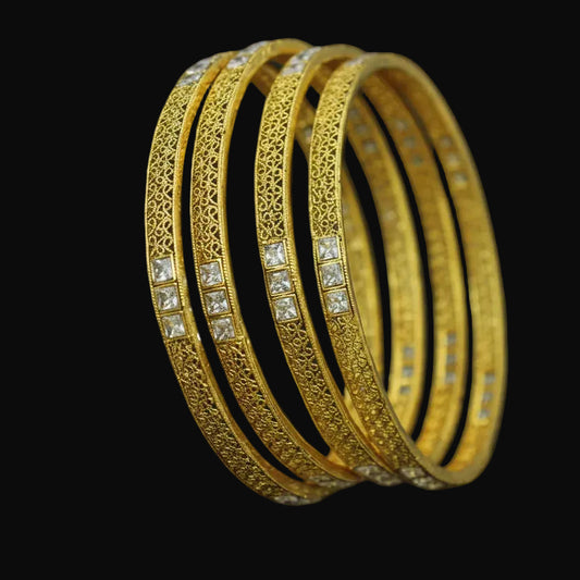 Gold bangles with intricate designs on a black stand, branded 'SAHELI'.