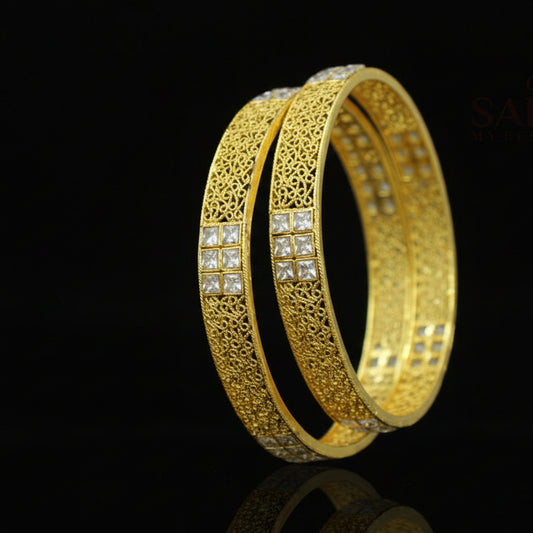 Gold bangles with intricate designs on a dark background, featuring the brand 'Saheli'.