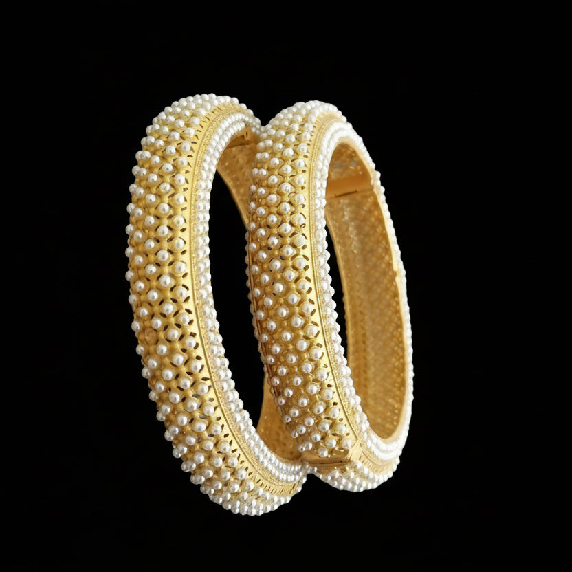Gold bangles with pearl detailing on a gray background, featuring the brand 'SAHELI'.