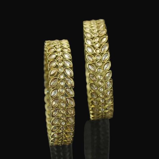 Pair of gold bangles with intricate designs on a dark background