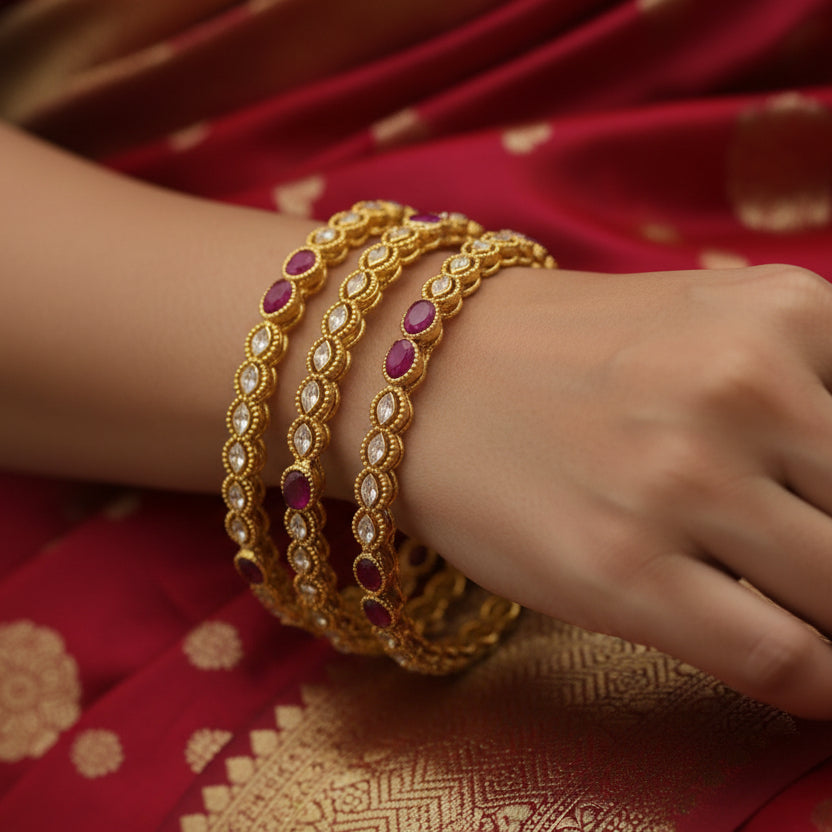 Gold bangles with red stones on a black stand, branded 'Saheli'.