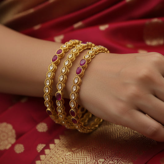 Gold bangles with red stones on a black stand, branded 'Saheli'.
