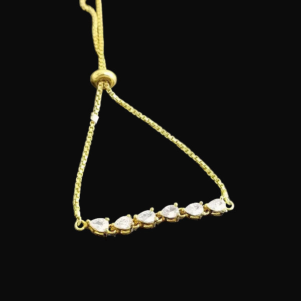 Gold bracelet with clear stones on a dark background, featuring the brand 'SAHELI'.