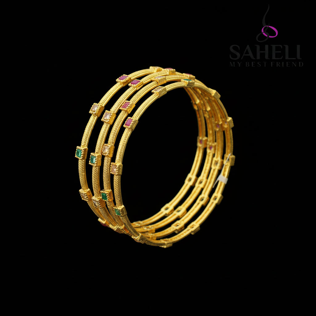 Gold bangles with gemstones on a black stand, branded 'SAHELI'.