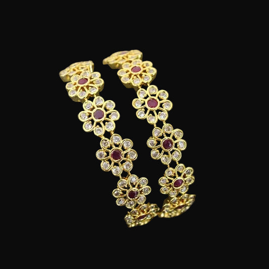 Gold bracelet with floral design and red gemstones on a gray stand against a dark background