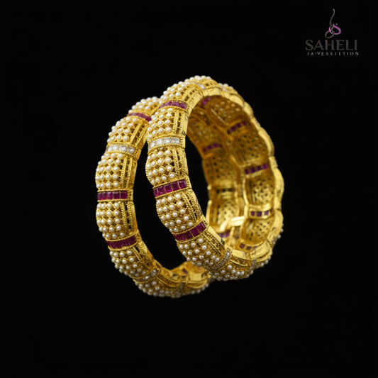 Gold bracelet with red stones on a reflective surface, branded 'Saheli'.