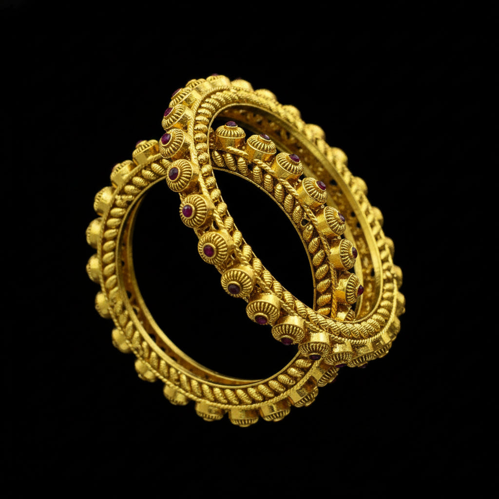 Gold bangles with red stones on a dark surface, branded 'Saheli'.