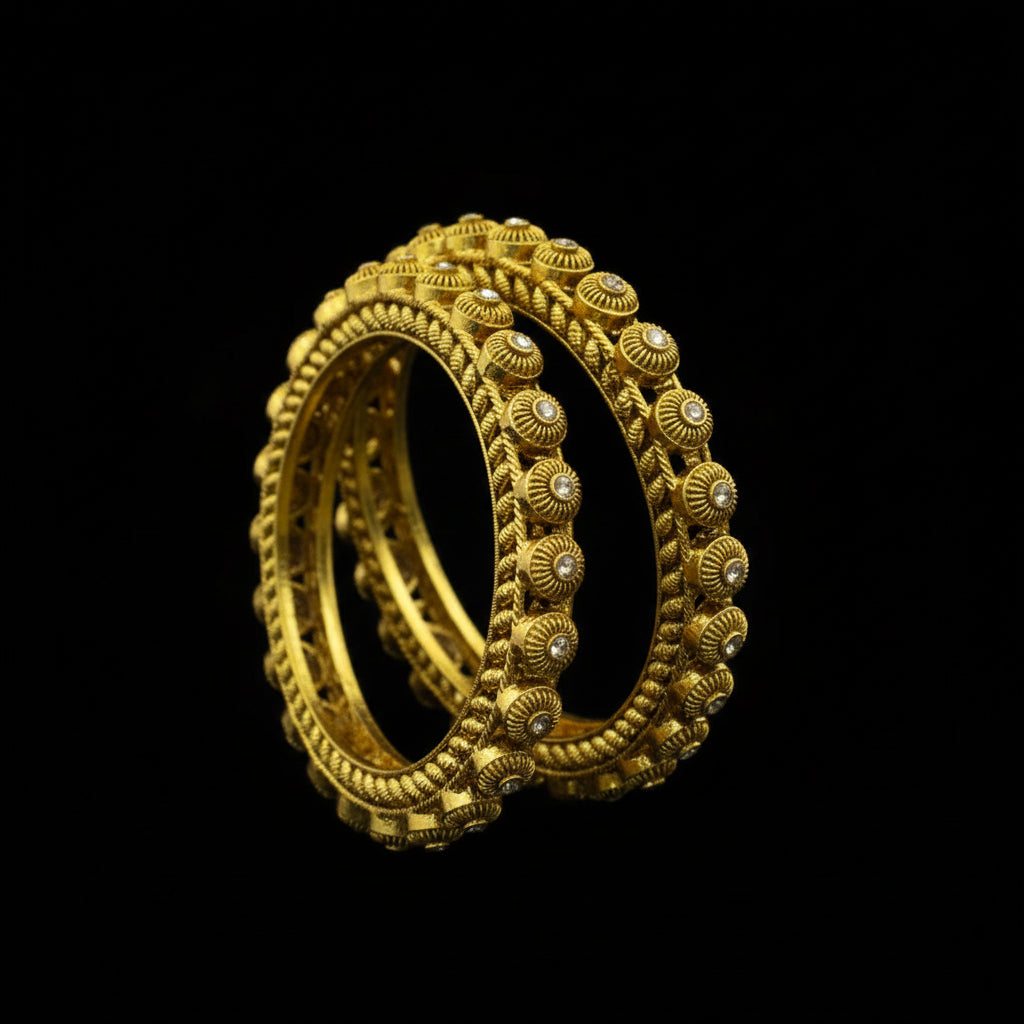 Gold bangles with intricate designs on a dark background, featuring the brand 'Saheli'.