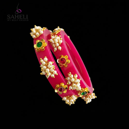 Pink bangles with gold and gemstone details on a gray background, branded 'SAHELI'.