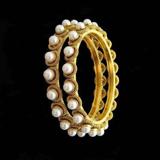 Gold and pearl bangles on a gray stand with 'SAHELI' branding.