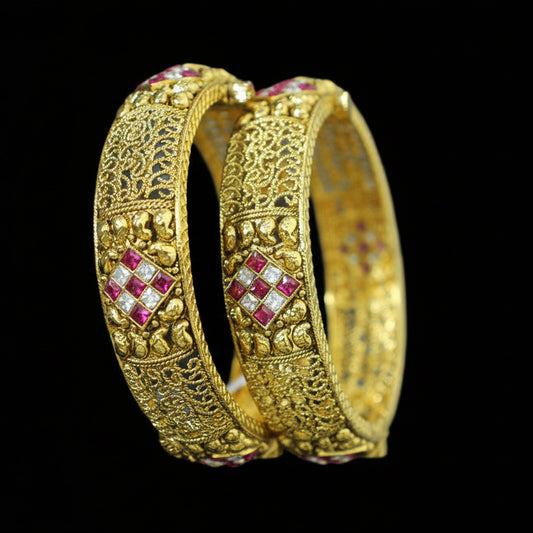 Gold bangles with red gemstones on a gray background, featuring the brand 'Saheli'.