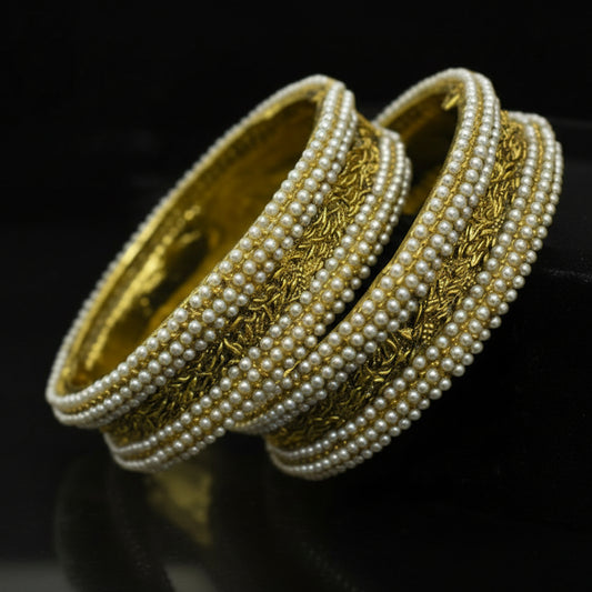 Pair of pearl bangles with gold accents on a reflective surface, featuring the brand 'Saheli'.