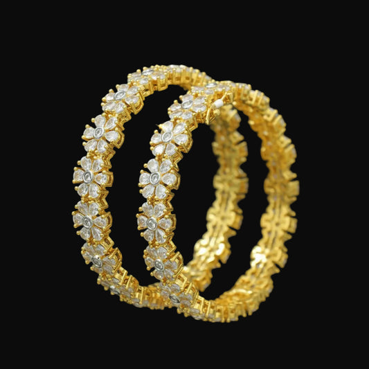 Gold bangles with floral design on a dark background, branded 'Saheli'.