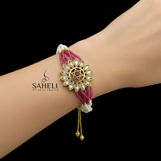 Decorative bracelet with pink and white beads and gold accents on a dark background, featuring the brand 'SAHELI'.