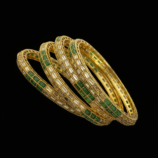 Gold bangles with green stones on a black stand, branded 'SAHELI'.
