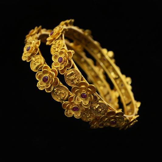 Gold bracelet with floral designs and red stones on a dark background, featuring the brand 'SAHELI'.