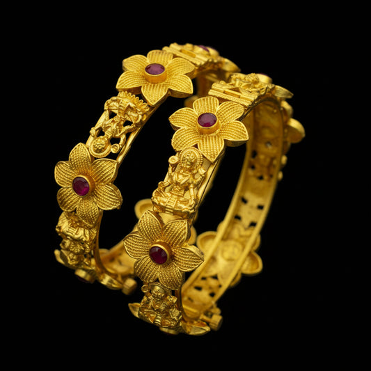 Gold bracelet with floral designs and red stones on a dark background