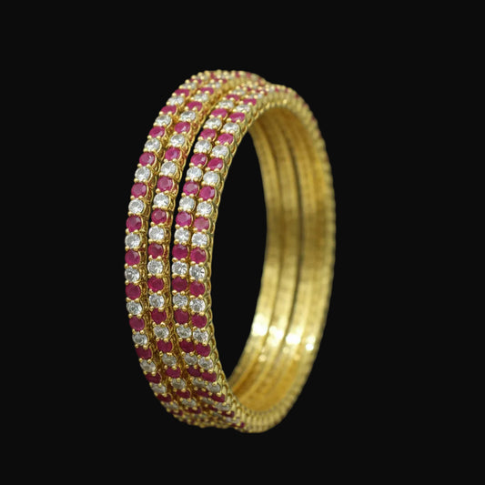 Gold bracelet with red and clear stones on a black background, branded 'Saheli'.