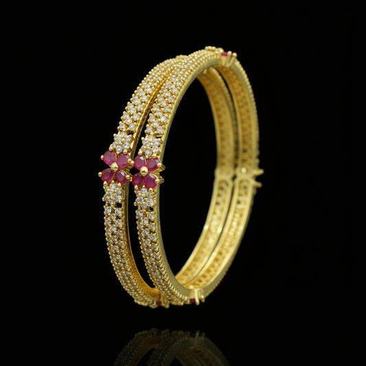 Gold bangles with pink stones on a black background, featuring the brand 'Saheli'.