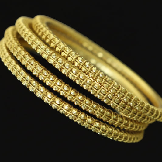 Gold bangles on a black stand with 'Saheli' branding in the corner.