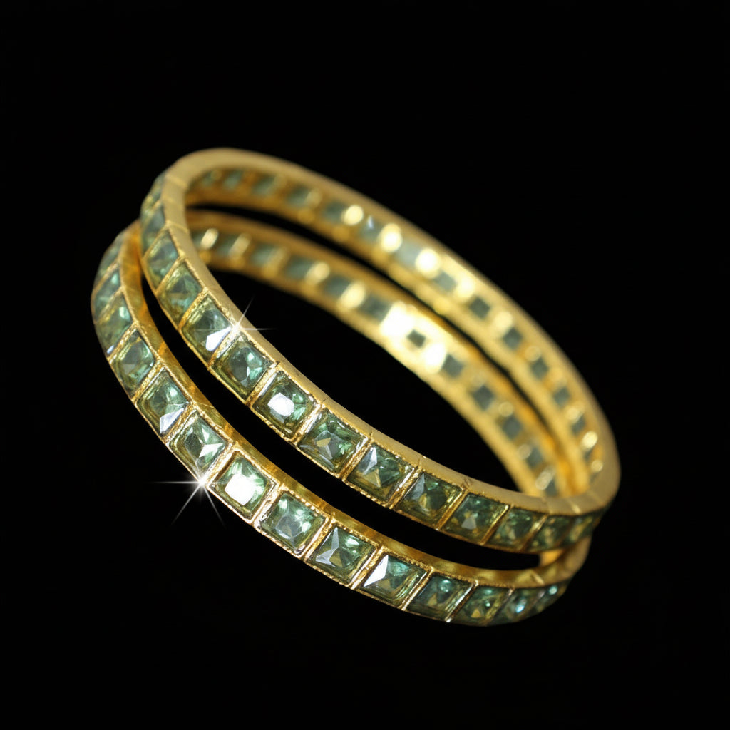 Gold bangles with green stones on a gray background, featuring the brand 'Saheli'.