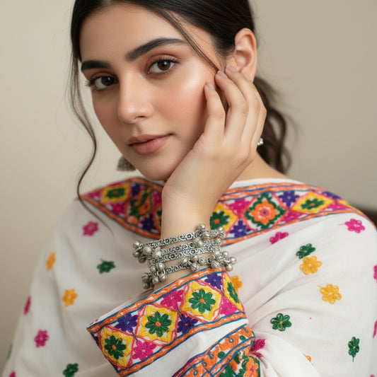 Silver bangles with intricate designs on a gray stand, branded 'Saheli'.