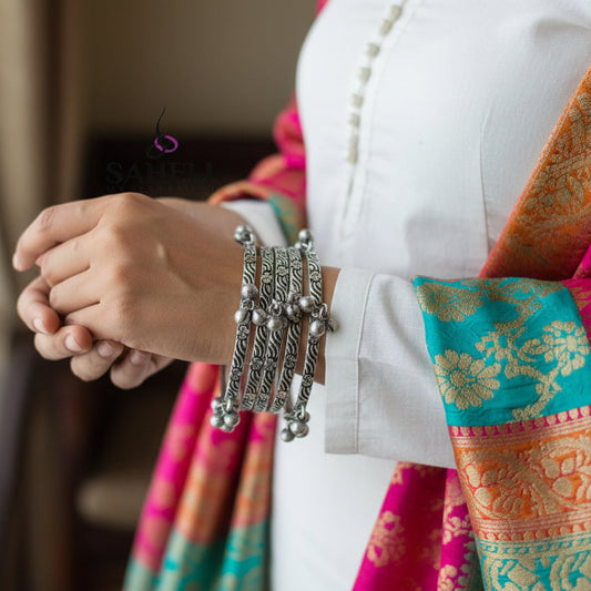 Set of silver bangles on a gray stand with 'SAHELI' branding.